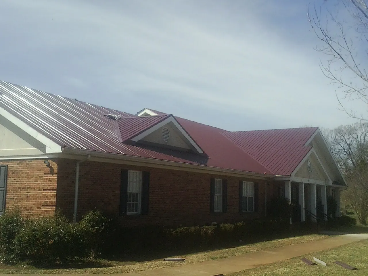 Red metal roof with gabled entries on a long brick building, from a Hail Damage Roof Repair job in Polk City