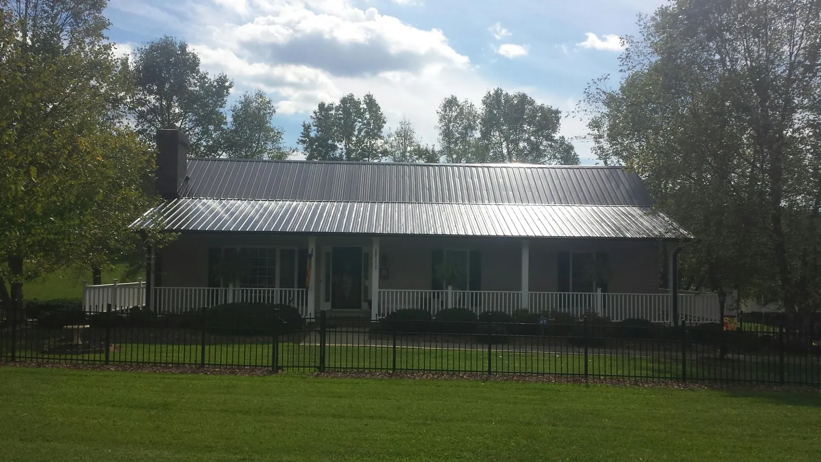 Gray metal roof on a brick ranch with a full width front porch — Gutter Guard Installation work by our crew in Polk City
