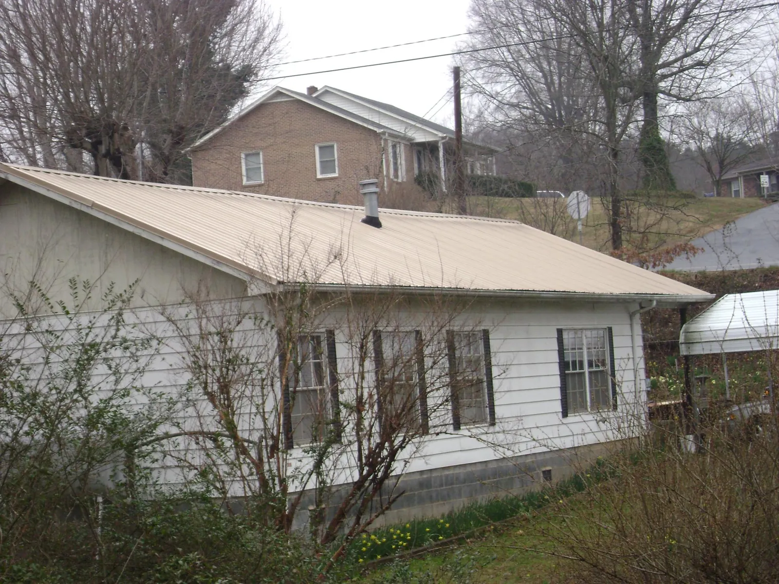 Tan metal roof on a white sided house set into a hillside — Commercial Roofing by Roofing Brothers in Polk City